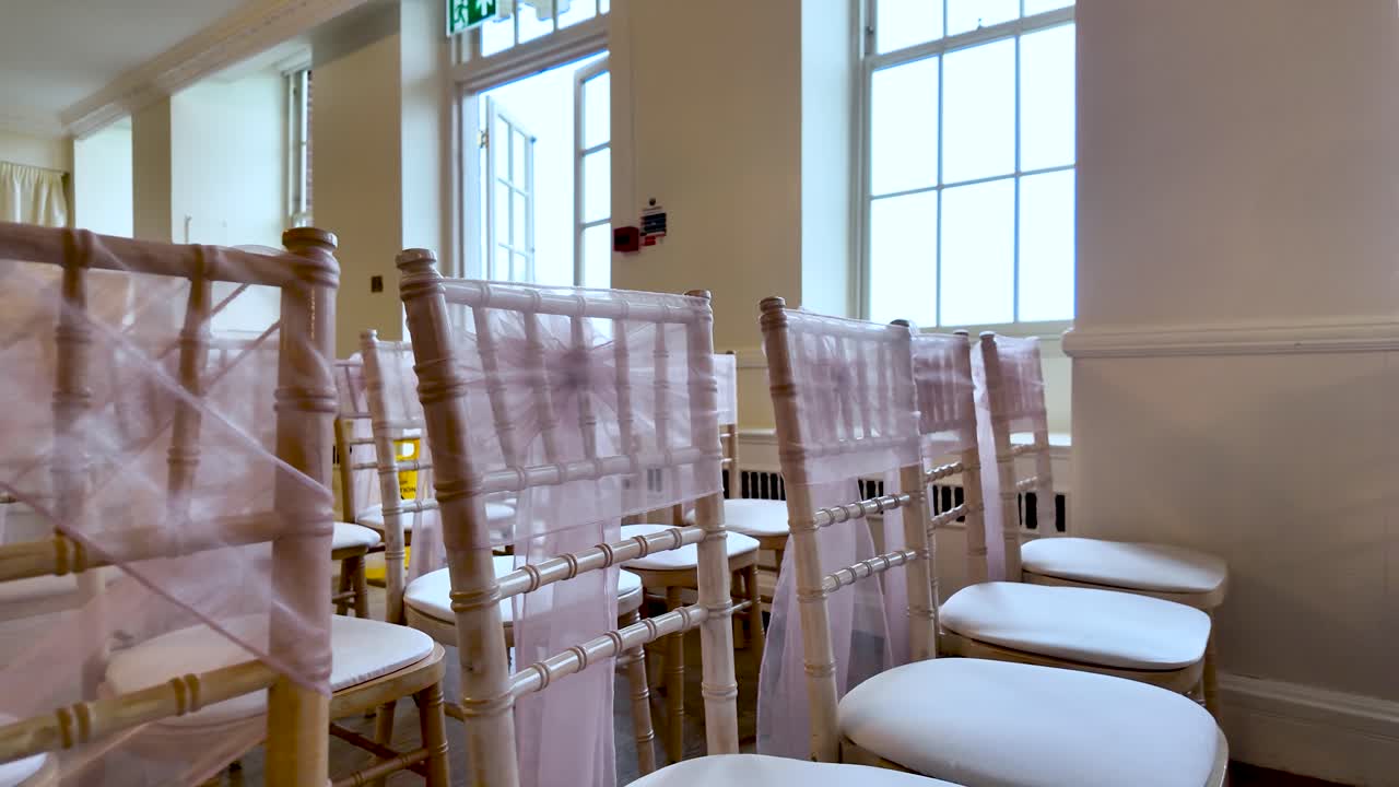 Filas de elegantes sillas decoradas con lazo rosa para una celebración de boda en un recinto.