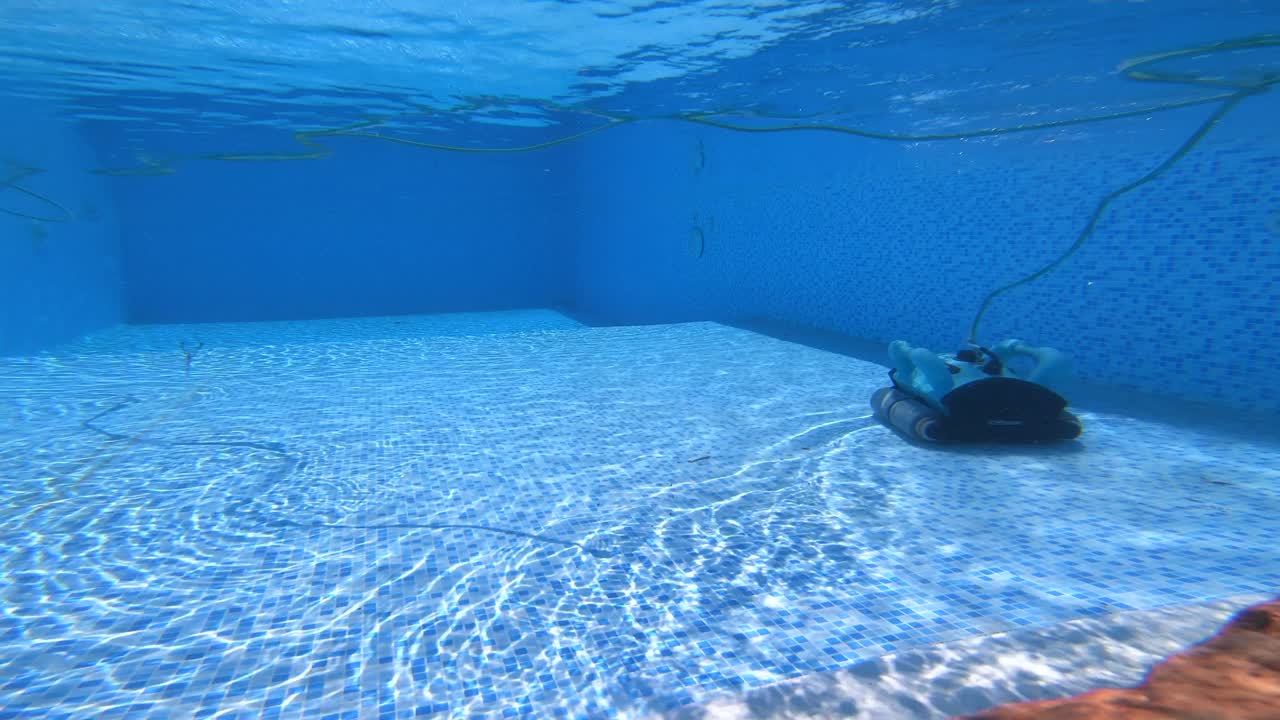 4K video of a pool cleaning device moving steadily across the bottom of a clear swimming pool—showing routine maintenance, clean water, and smooth equipment operation on a sunny day.