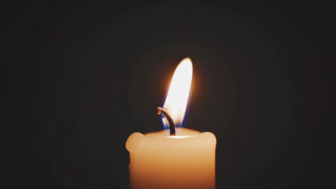 Detailní video zapálené svíčky na tmavém pozadí. Přímý úhel kamery.