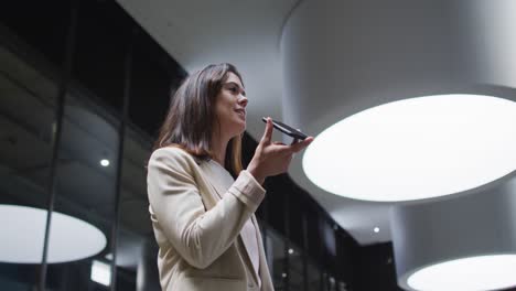 mujer de negocios caucásica usando un teléfono inteligente en el vestíbulo de una oficina moderna