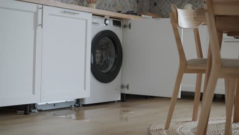 water leaking from a washing machine in a contemporary kitchen setting, showing a puddle on wooden flooring