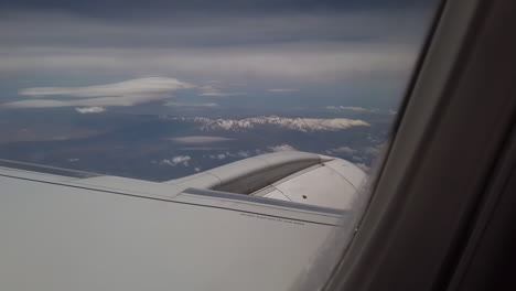 man's finger showing snow-capped mountains through the window of an airplane