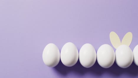 White-easter-eggs-with-rabbit-ears-on-purple-background-with-copy-space