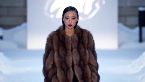 a stunning fashion model walks gracefully in a luxurious brown fur coat on a snowy runway, showcasing elegance and sophistication in a winter wonderland