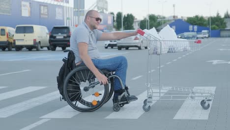 man with disabilities in wheelchair pushing cart in front of himself at supermarket parking