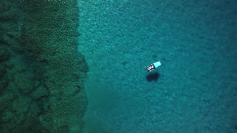 Static-aerial-view-of-a-boat-floating-on-crystal-clear-blue-water-above-a-beautiful-coral-reef