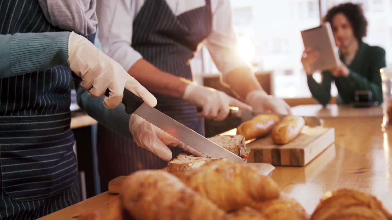 웨이터 와 웨이트리스 가 카운터 에서  ⁇   ⁇  과 샌드위치 를 자르고 있다
