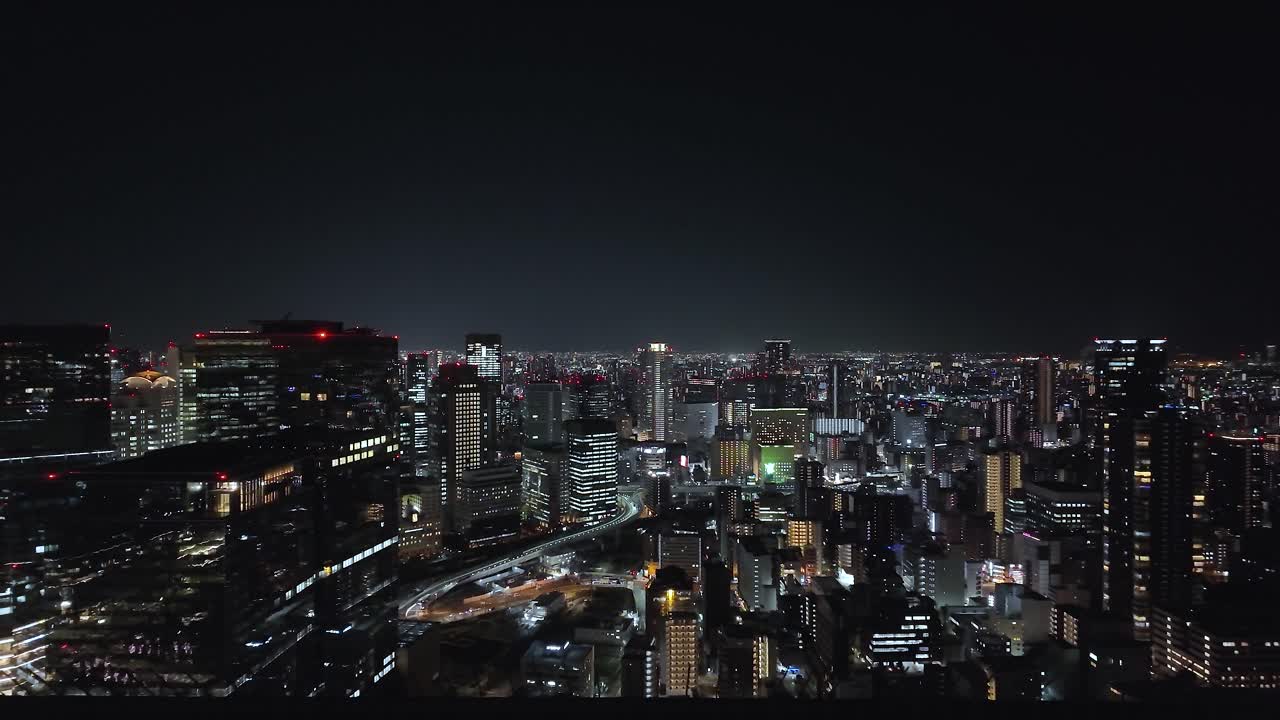 High angle view of illuminated Osaka cityscape at night, showing skyscrapers, offices and roads