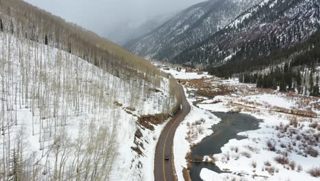 lonely car ride on country road in between massive mountain ranges, aerial drone view