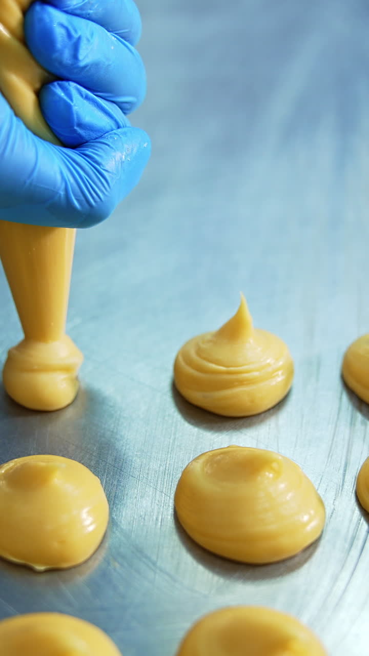 Yellow liquid pastry dough being squeezed on the baking sheet. Close up. Pastry production at confectionery factory. Vertical video