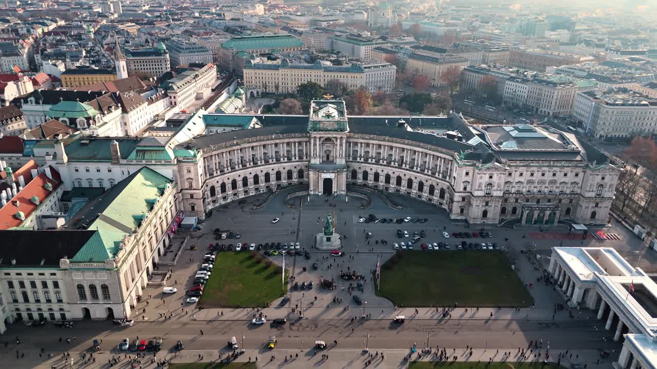 Ripresa aerea statica con drone del Palazzo Hofburg a Vienna, che mostra il palazzo, il paesaggio urbano circostante, la luce del tramonto invernale, il cielo nuvoloso e i turisti che passeggiano nel parco del palazzo sottostante