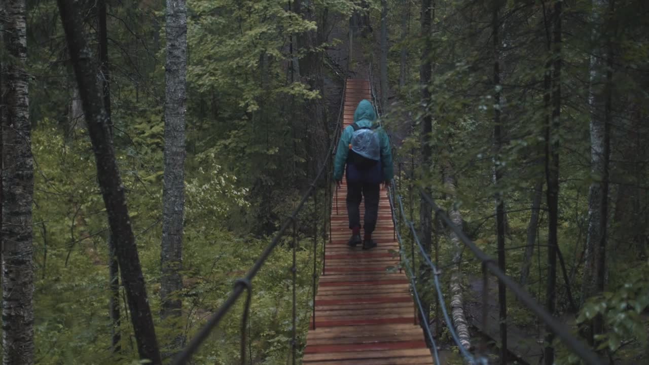 persona caminando en un puente colgante de madera en un bosque