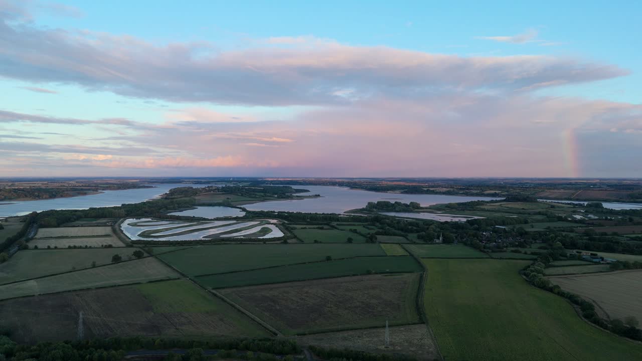 Aerial footage of Rutland Water Reservoir in England with rainbow at sunset during tranquil blue hour over scenic countryside landscape