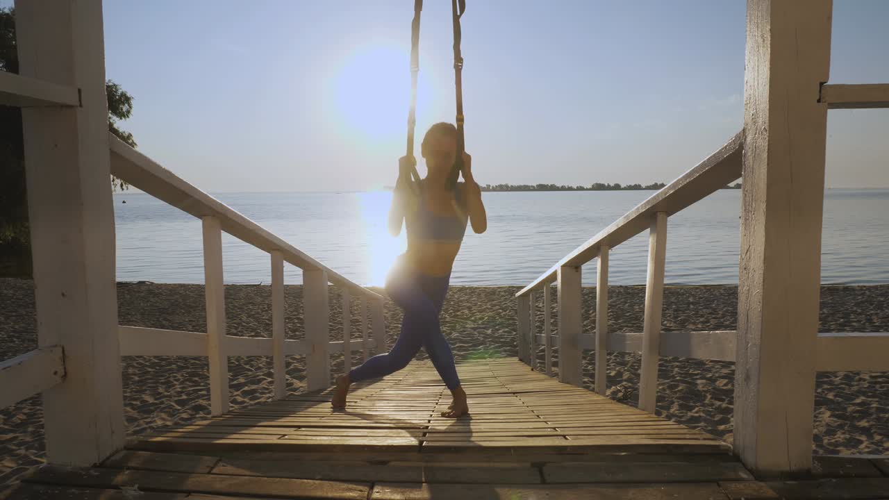 entrenamiento al aire libre. correas de suspensión. entrenamiento con correas. mujer joven atlética está haciendo ejercicios de resistencia de todo el cuerpo usando cuerdas en bucle trx, en la playa durante la puesta o el amanecer. entrenamiento de fitness al aire abierto. concepto de estilo de vida saludable. deporte matutino