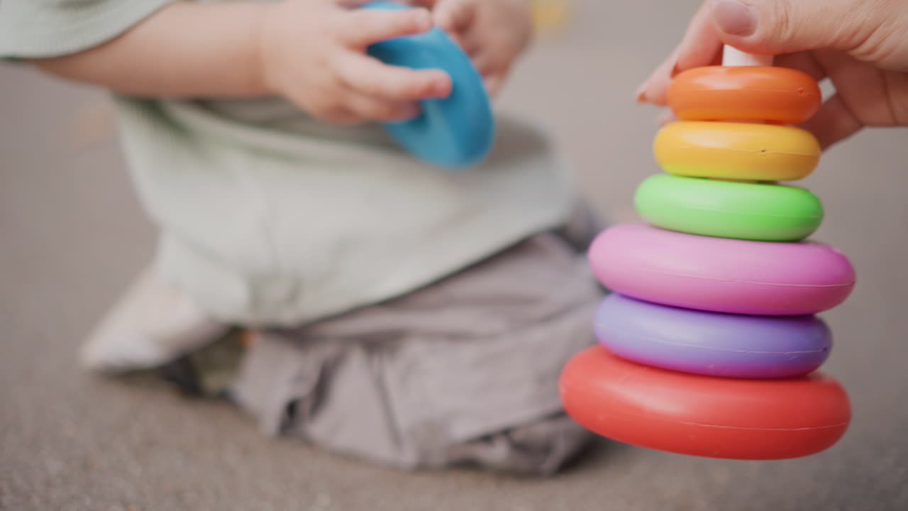 屋外で微細運動能力を練習する幼児。大人の手助けを受け、鮮やかなリングを積み重ねる小さな子供。屋外で大人の指導のもと、微細運動能力の発達に取り組む白人の幼児。