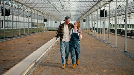 happy guy in a plaid shirt walks along the greenhouse with his farmer girlfriend and discuss their plans to work in the greenhouse on the farm