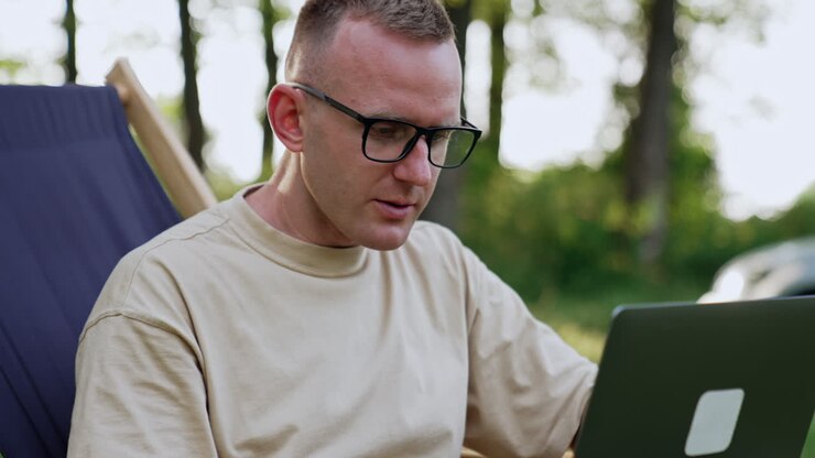 Busy man working remote in nature. Freelancer in glasses focused on work having some difficulties.