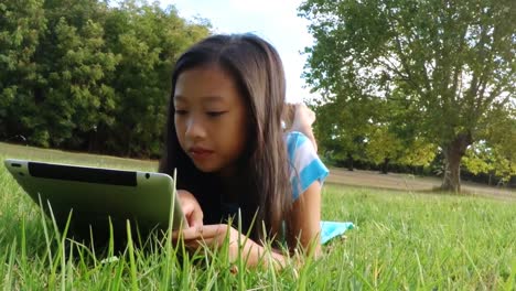 Lächelndes-Mädchen,-Das-Auf-Gras-Liegt-Und-Ein-Digitales-Tablet-Benutzt