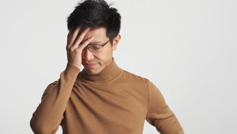 Annoyed-Asian-man-in-eyeglasses-covering-his-face.