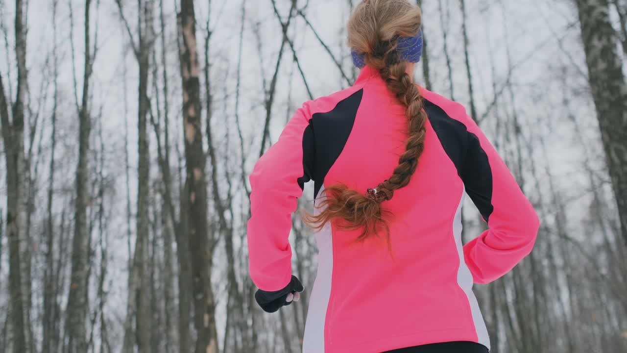 una joven corre por el parque en invierno con una chaqueta rosa. vista desde atrás