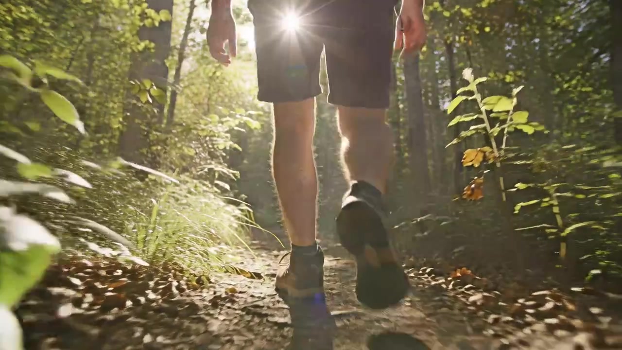 Caminhante adulto dando o primeiro passo por uma trilha estreita na floresta, vestindo shorts escuros e sapatos de caminhada