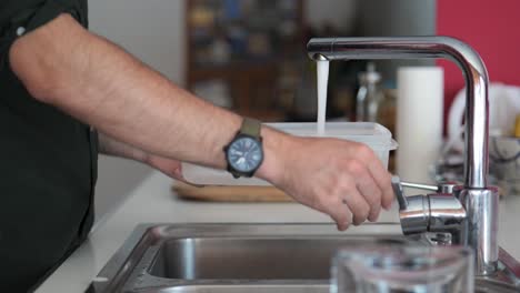 filling a plastic container with water in the sink of the kitchen