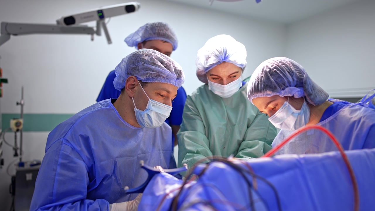 Chirurghi concentrati sul campo operatorio in neurochirurgia. Squadra in camici blu e verde acqua si china sul telo chirurgico, braccio di neuronavigazione visibile in alto a sinistra