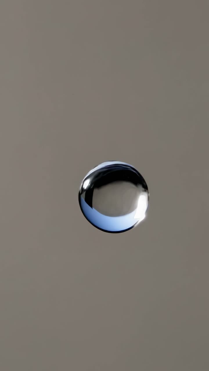 A minimalist video still of a single water droplet suspended mid-air, captured from a side angle
