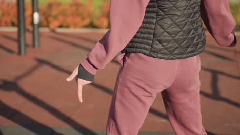 waist view of sportswoman in hoodie swaying side to side in lunge stance on outdoor court, long shadows cast across rubber tiles, autumn foliage glowing under sun around workout bars