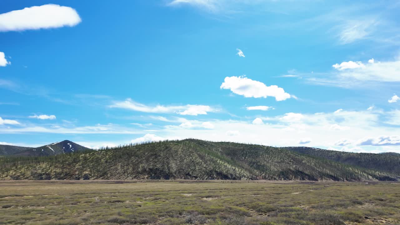 una vista de las montañas siberianas en un día soleado de verano con un cielo azul brillante y nubes blancas