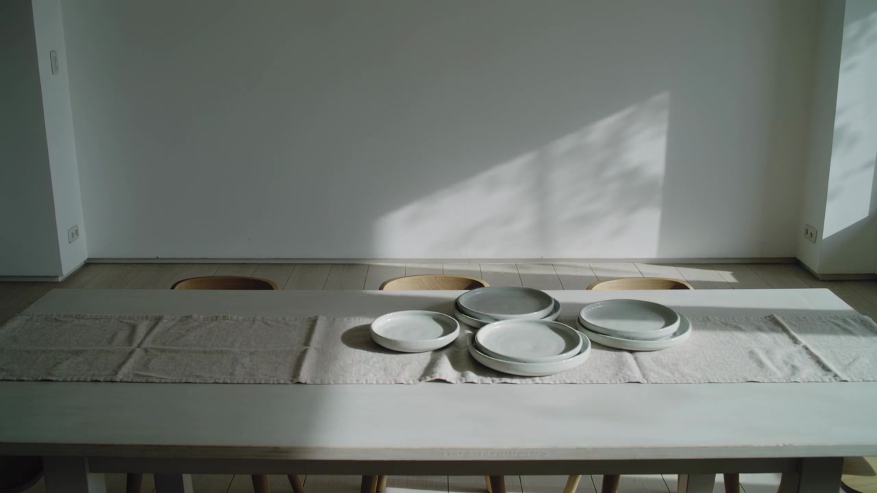 Luce solare mutevole proveniente dalla finestra destra che si sposta lungo un lungo tavolo da pranzo in casa, alterando le ombre dei piatti