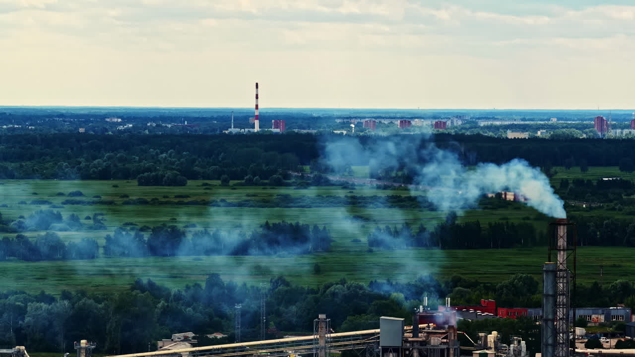 Factory smoke drifts across green fields toward the outskirts of Riga with chimneys on the horizon