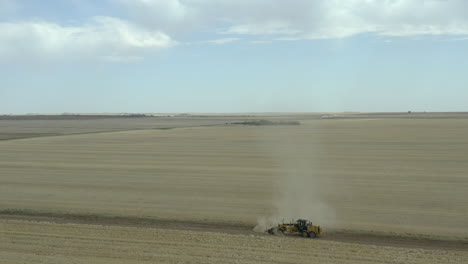 motoniveladora creando superficie plana en camino de tierra con nube de polvo, rural