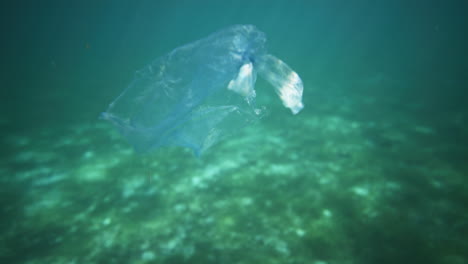 plastic bag floating in crystal clear water with light reflections shot from underwater