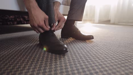 hands of man groom adjusting, wearing, putting his wedding shoes in hotel room near window