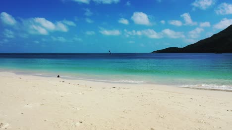 Paradise-white-sandy-beach-washed-by-waves-of-blue-turquoise-sea-under-bright-sky-with-white-clouds-on-tropical-seaside-in-Thailand