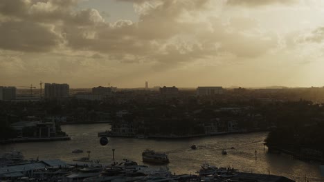 Puesta-De-Sol-Sobre-Una-Ciudad-Costera-En-Florida,-Barcos-En-El-Agua-A-Lo-Lejos-Y-Sol-Brillando-A-Través-De-Las-Nubes