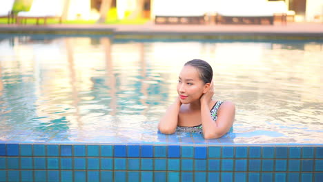 A-young,-pretty-woman-pushes-her-wet-long-hair-back-from-her-face-as-she-finishes-a-relaxing-swim-in-a-resort-pool
