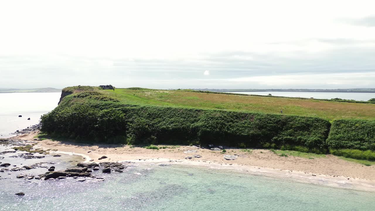 Sunny Welsh Penrhos coastal meadow headland overlooking rocky seafront beach aerial view
