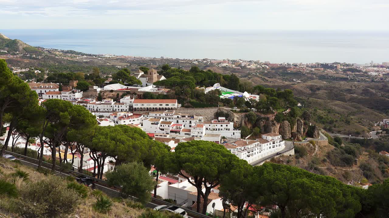 Traffic passes by the outskirts of the famous white town of Mijas with the Costa del Sol and Mediterranean Sea in the distance. Spain