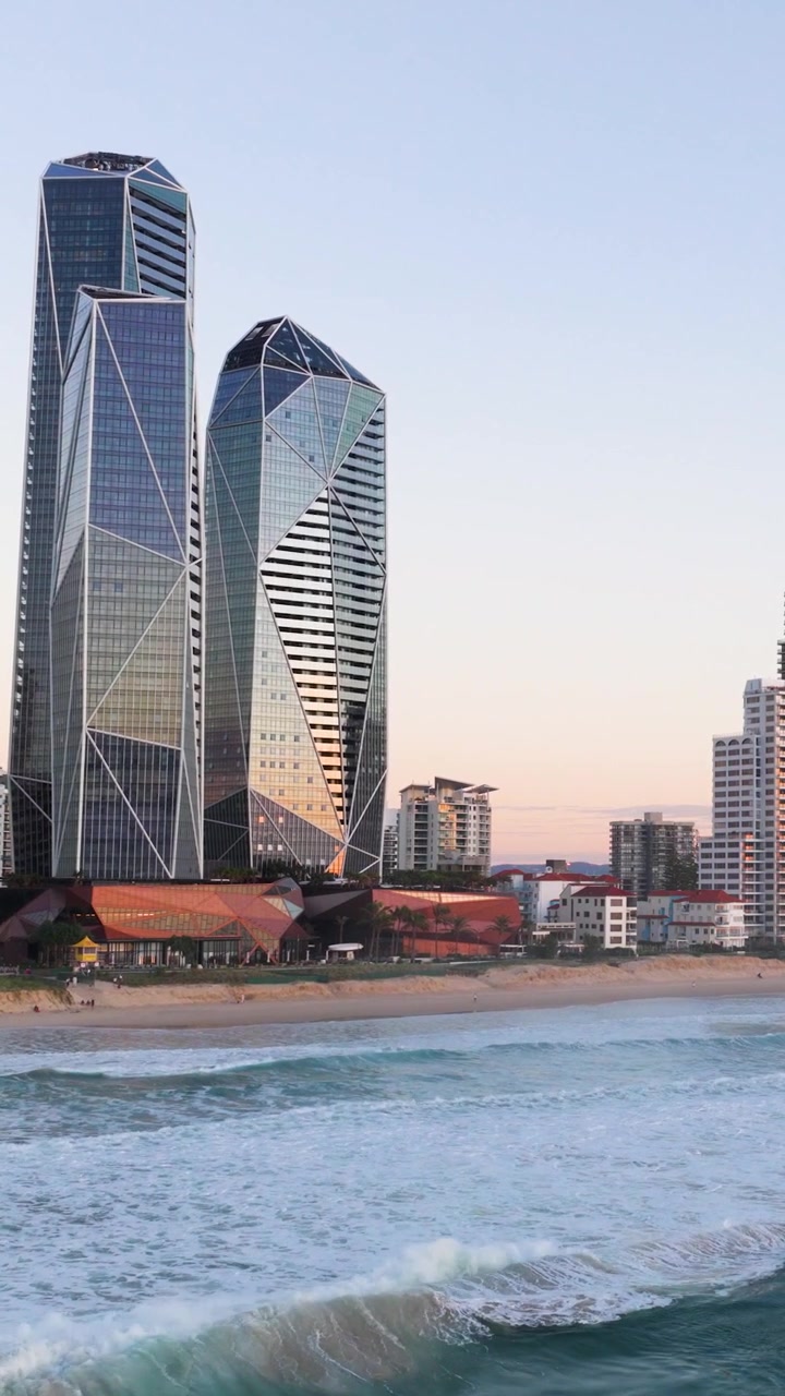 Skyscrapers overlook the ocean as waves crash on the Gold Coast beach at sunset, creating a serene urban-seaside contrast