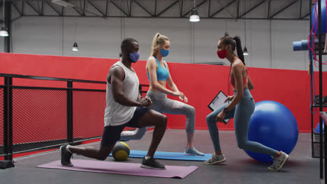 Diverse-group-doing-lunges-wearing-face-masks-at-gym