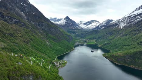 Stunning-Geiranger-Norway-listed-on-Unesco-World-Heritage---Beautiful-aerial-with-Ornevegen-road-on-left-and-Geiranger-in-background-surrounded-by-mountain-scenery-and-a-cruise-ship-on-Geirangerfjord