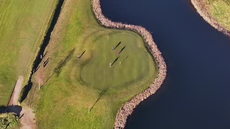 aerial video of a golf club in ireland showing golfers shadows playing on the green by a lake