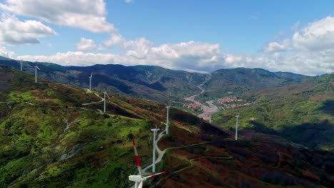 tilt down view of white windmills moving over hilly terrain with white clouds passing by on a bright sunny day