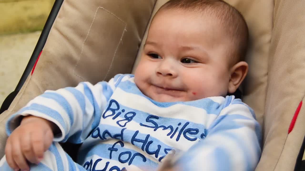 clip de primer plano de un bebé con un mono de rayas azules sonriendo a alguien fuera de cámara