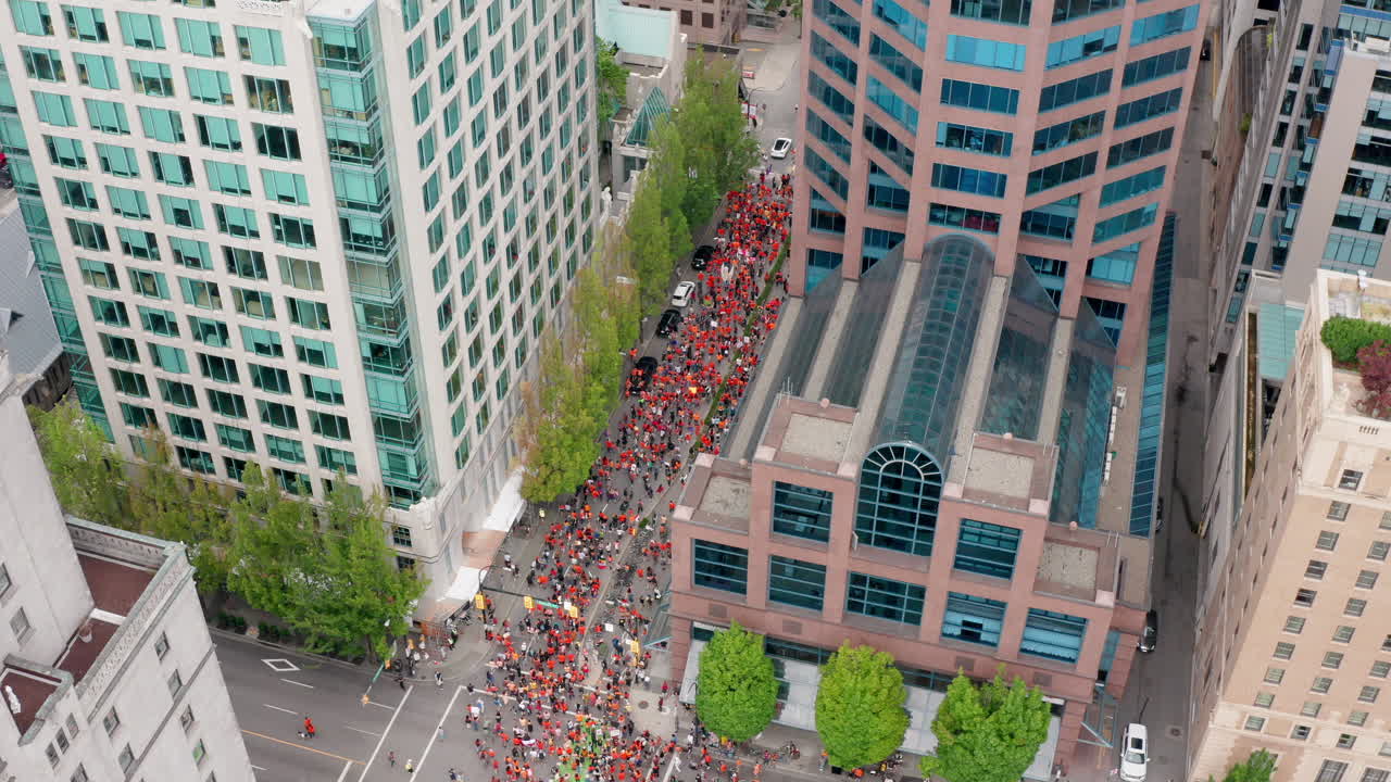 una multitud masiva de personas marcha en la calle de la ciudad, revelan drones de arriba hacia abajo