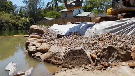 una excavadora que utiliza un agarrador de rocas para construir un muro de rocas a lo largo de un río