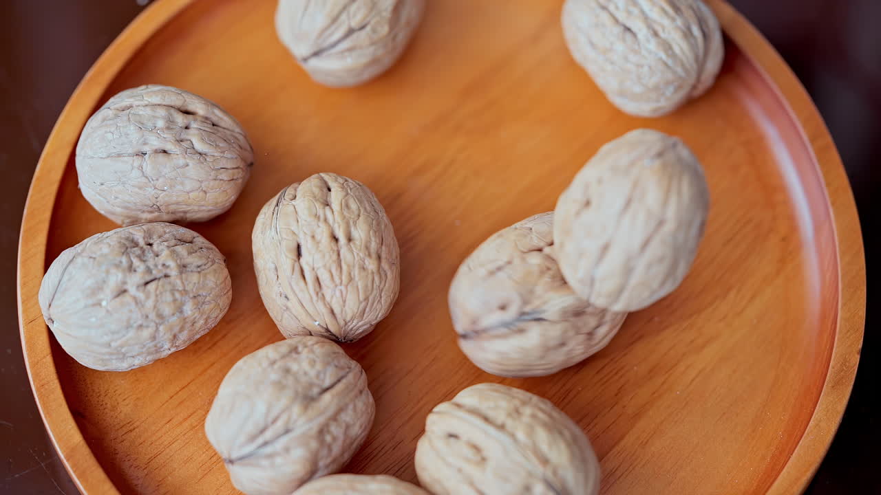 In a beautiful light, walnuts fall into the wooden plate in slow motion, top view and close up shot