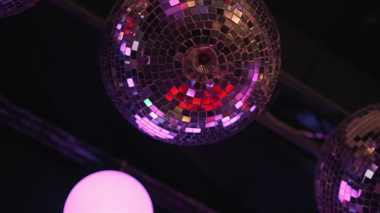 Ripresa dal basso di una sfera da discoteca a specchi rotante che riflette luci colorate di club, creando un'atmosfera festosa di vita notturna